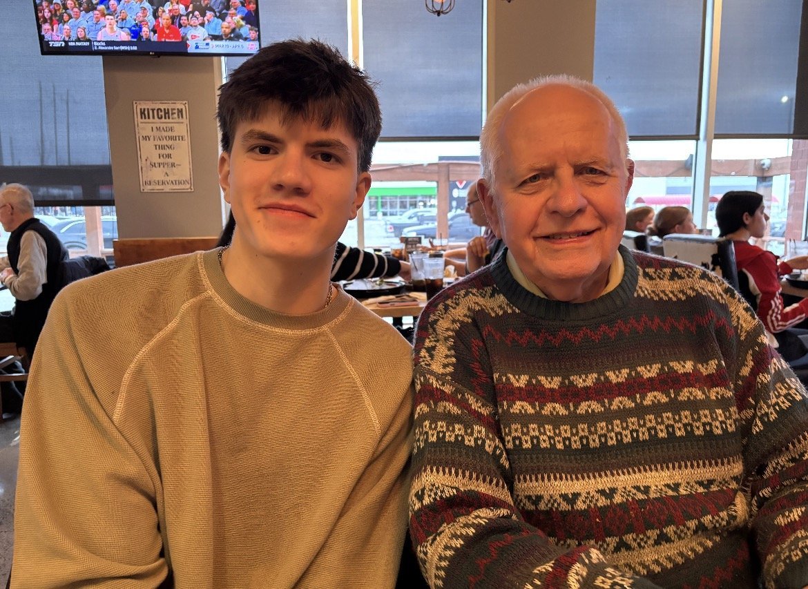 Owen Nitta Mackay sitting beside his grandfather at a restaurant table, both smiling at the camera.